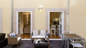 A cozy outdoor seating area with wicker furniture, a wooden table, and a view into the adjacent kitchen. - Studio with courtyard, at 3 min walking from the beach and 20 from center by BUS (Porto)