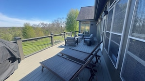 Une terrasse dotée de mobilier d’extérieur, d’un barbecue couvert et offrant une vue sur un paysage verdoyant.