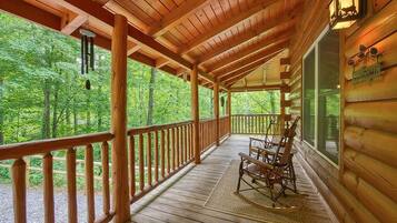 A wooden cabin with a porch, rocking chairs, and a welcome sign.