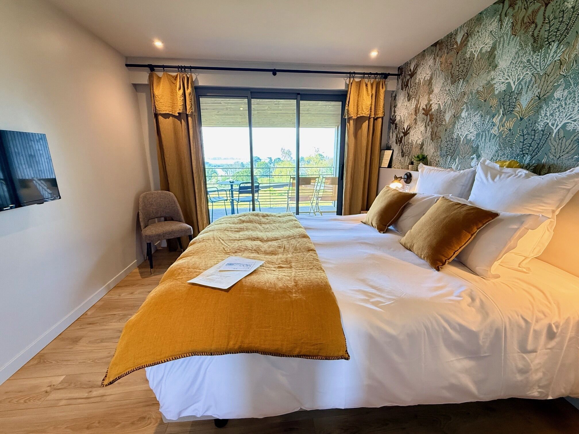 Une chambre à coucher avec un grand lit, une chaise, un bureau et une vue sur l’extérieur.