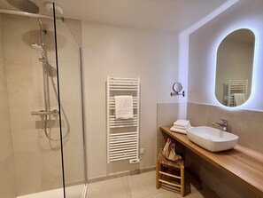A modern bathroom with a glass shower enclosure, a white towel rack, a wooden vanity with a sink, and a mirror. - La Bellevue Bistrot et Chambres D'hotes (Sene)