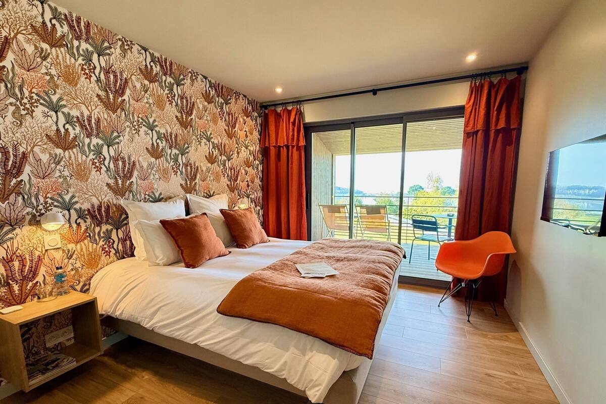 A bedroom with a bed, a nightstand, a chair, and a view of the outdoors.