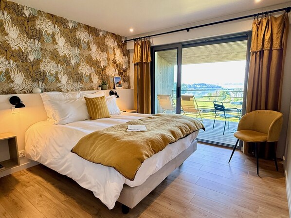 Un dormitorio con una cama grande, una mesita de noche, una silla, un balcón con vistas y una pared con diseño.