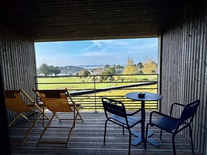 A balcony with a view of a green field and a lake. There are two chairs and a small table. - La Bellevue Bistrot et Chambres D'hotes (Sene)