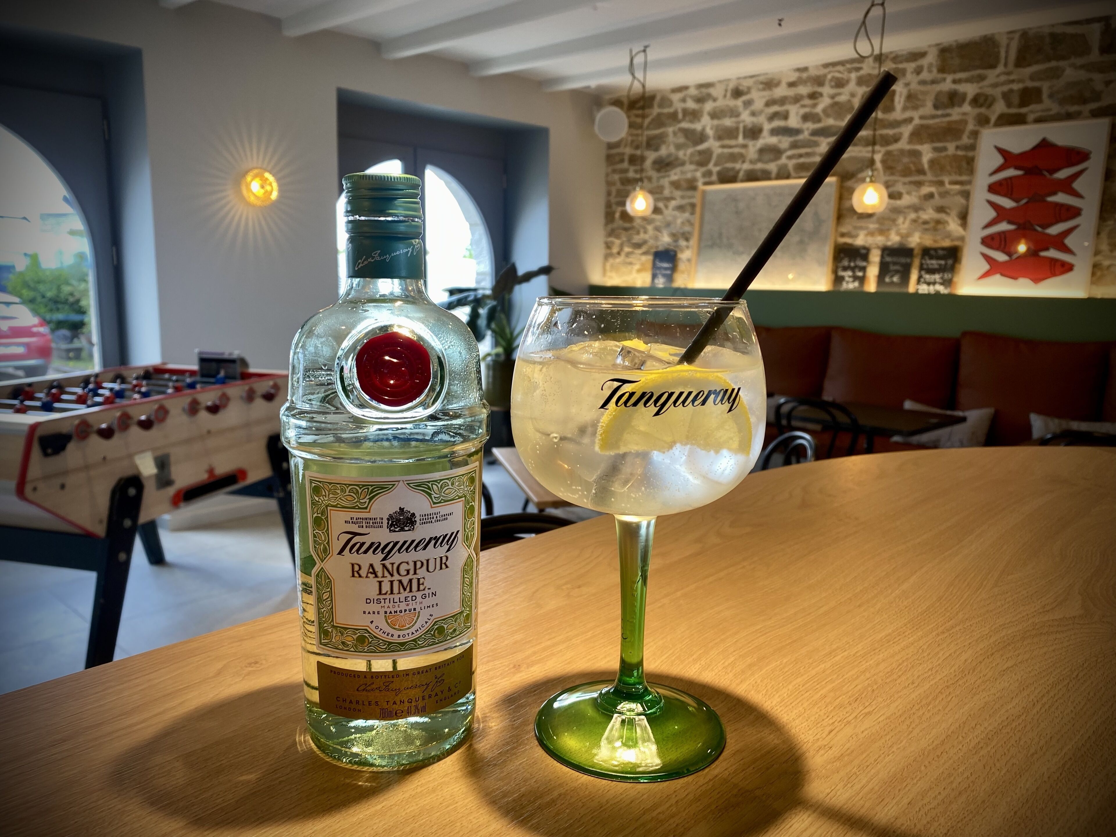 Une bouteille de gin Rangpur Lime et un verre de cocktail Tanguray sur une table en bois dans un restaurant.
