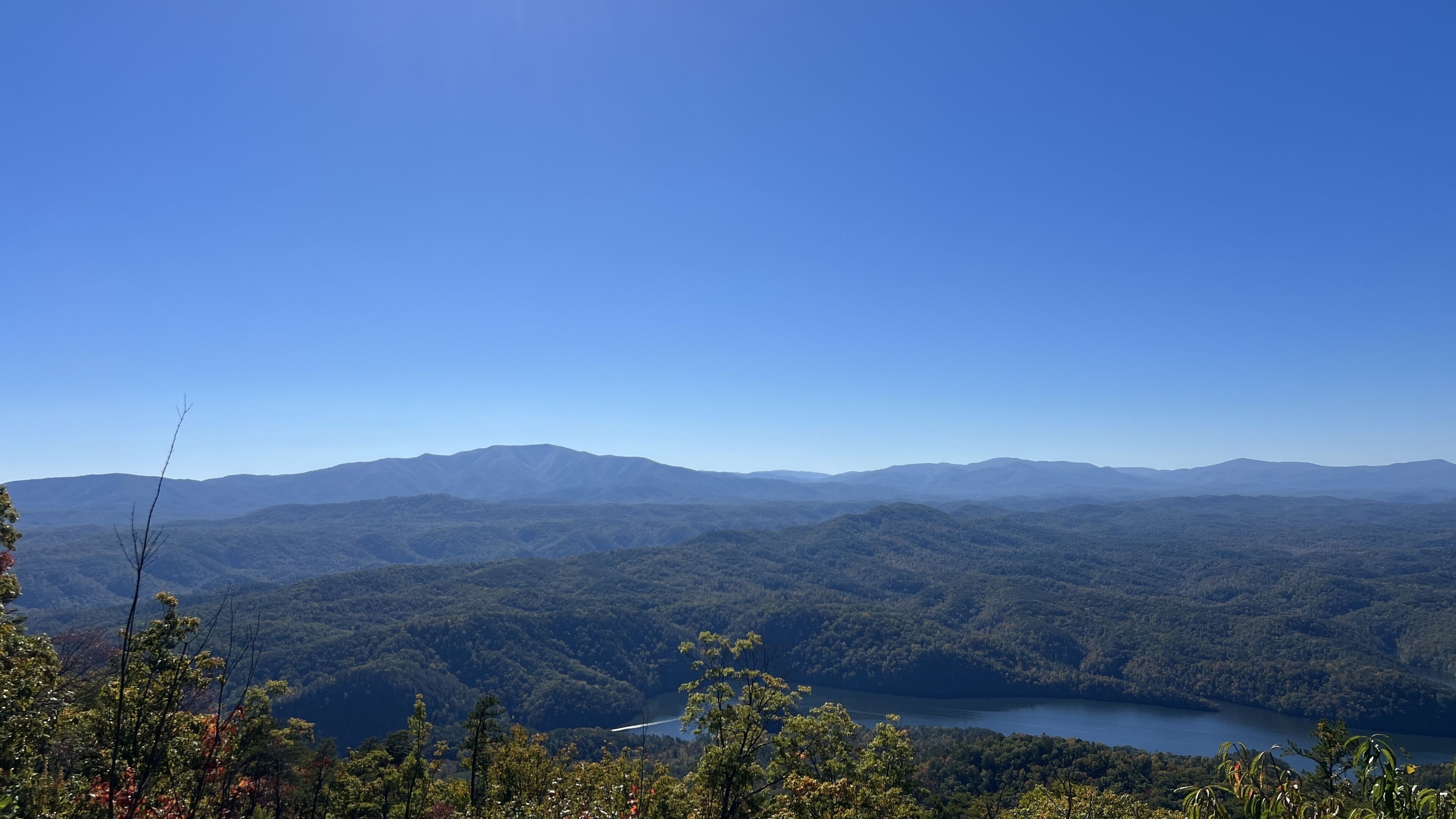 Une vue panoramique d’un paysage montagneux, avec un lac au premier plan et un ciel bleu dégagé.