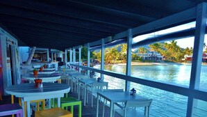 An outdoor dining area with tables and chairs, overlooking a body of water with buildings and trees in the background. - Point Pleasant - Perfect Romantic Getaway - 3 Pools/Intimate Beach (St Thomas)
