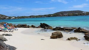 A beach with clear turquoise water, rocky shoreline, and a few people sunbathing. - Point Pleasant - Perfect Romantic Getaway - 3 Pools/Intimate Beach (St Thomas)
