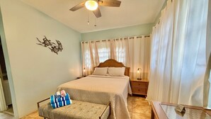 A bedroom with a bed, a nightstand, a bench, a ceiling fan, and a wall decoration. - Point Pleasant - Perfect Romantic Getaway - 3 Pools/Intimate Beach (St Thomas)