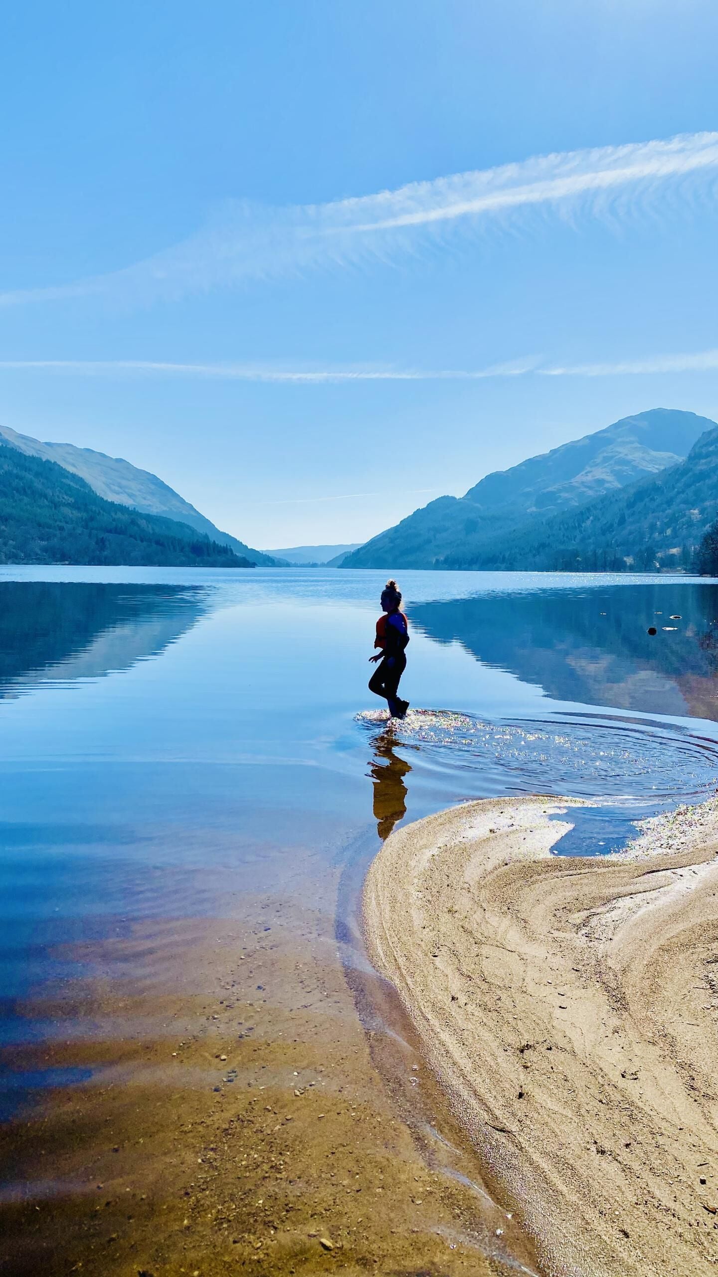 Eine Person geht über eine spiegelnde Wasseroberfläche, im Hintergrund Berge.