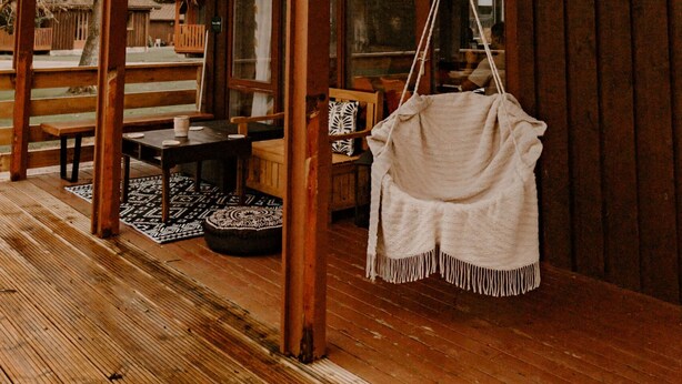 A wooden cabin with a covered porch, a hanging chair, and a dining area with a table and benches. - Luxurious Mountain Retreat Lodge Hunters Quay (Dunoon)