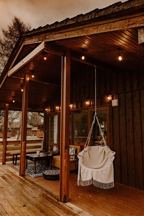 A wooden cabin with a covered porch, a hanging chair, and a dining area with a table and benches. - Luxurious Mountain Retreat Lodge Hunters Quay (Dunoon)