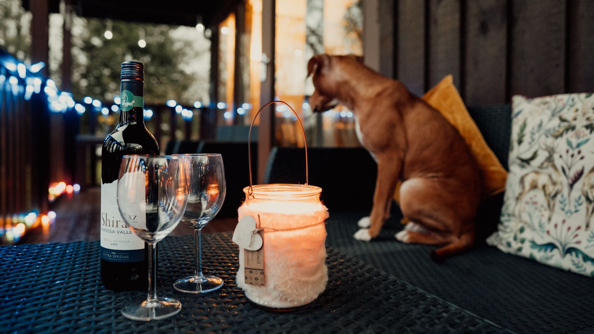 A bottle of wine, two wine glasses, and a candle on a table.