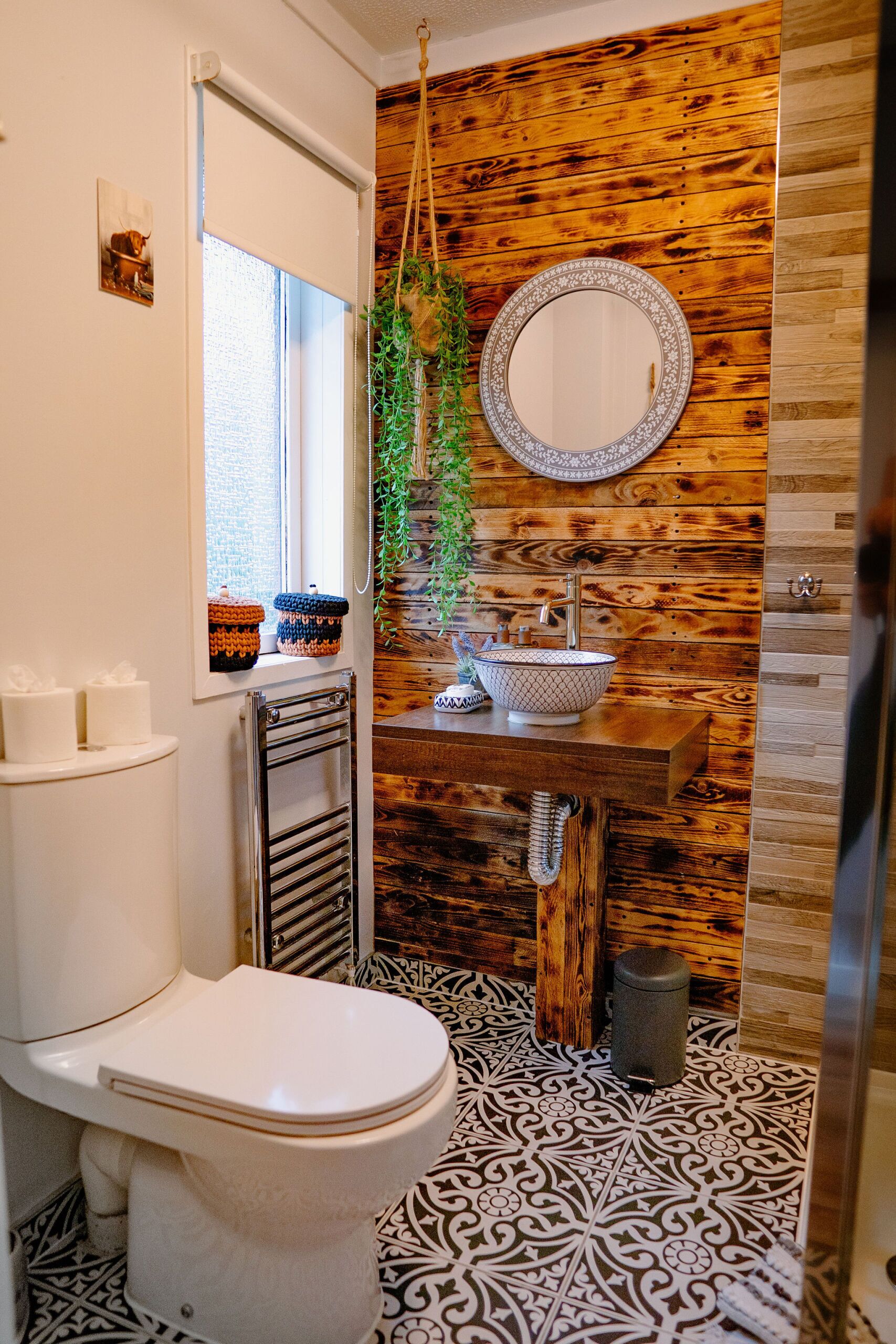 A bathroom with a wooden wall, a sink with a mirror, a toilet, and patterned floor tiles.