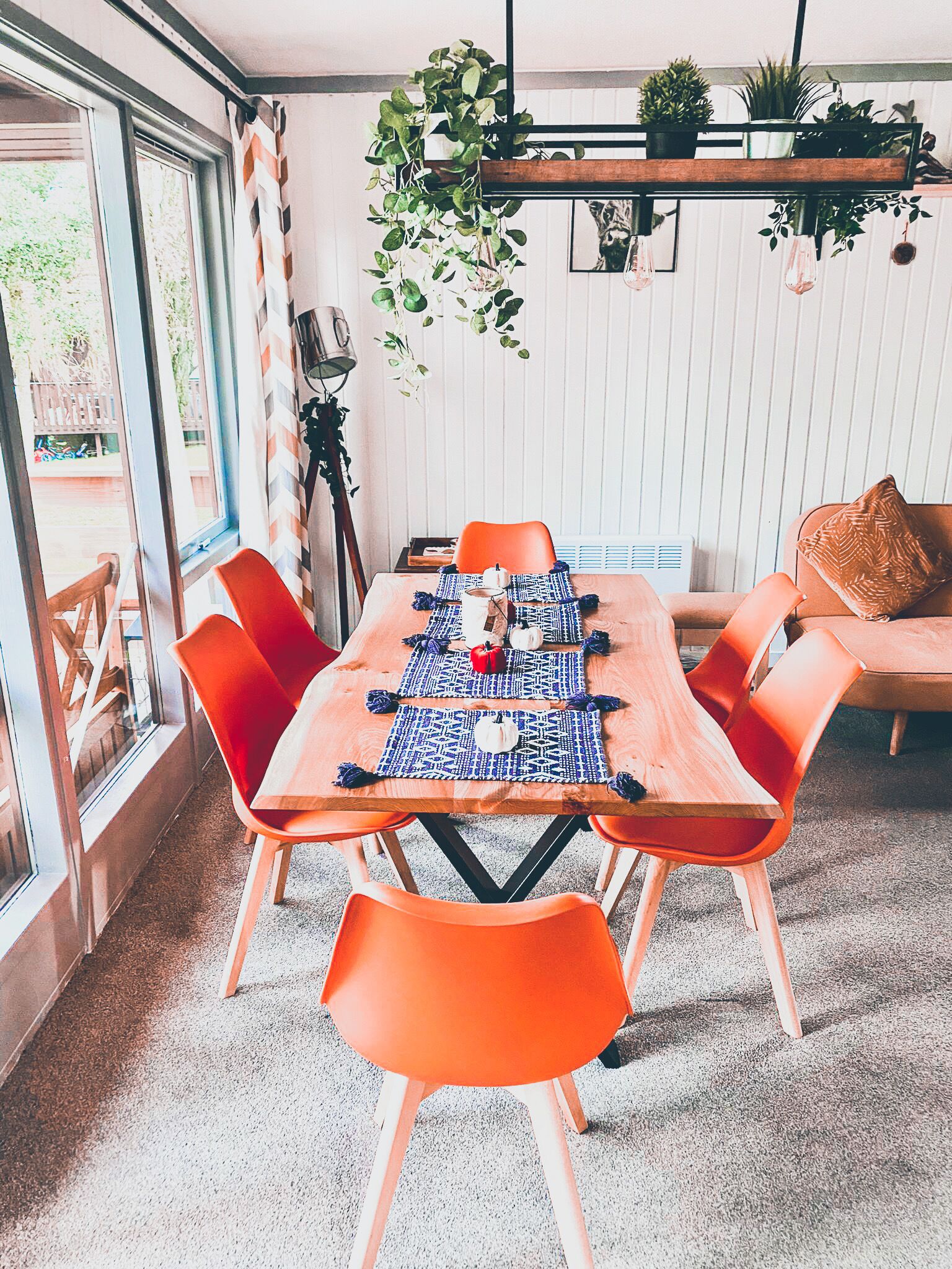A dining area with a wooden table, orange chairs, and a hanging plant.