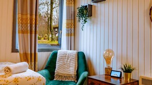 A cozy room with a bed, a green armchair, a wooden nightstand, and a window with curtains. - Luxurious Mountain Retreat Lodge Hunters Quay (Dunoon)