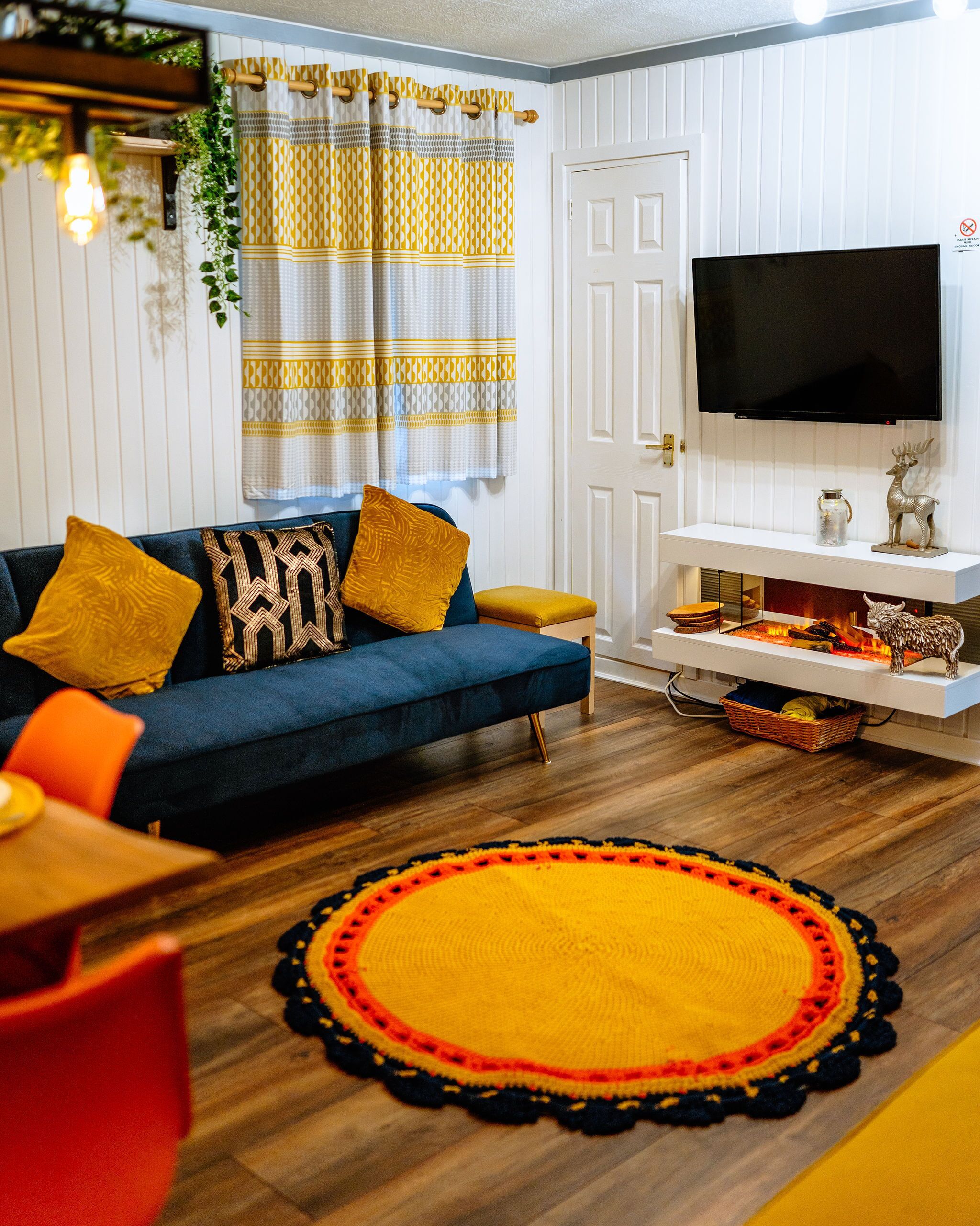 A living room with a blue sofa, yellow cushions, a flat-screen TV, a fireplace, and a round rug.
