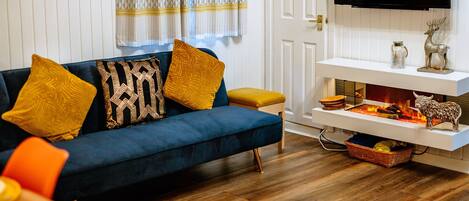 A living room with a blue sofa, yellow cushions, a flat-screen TV, a fireplace, and a round rug.