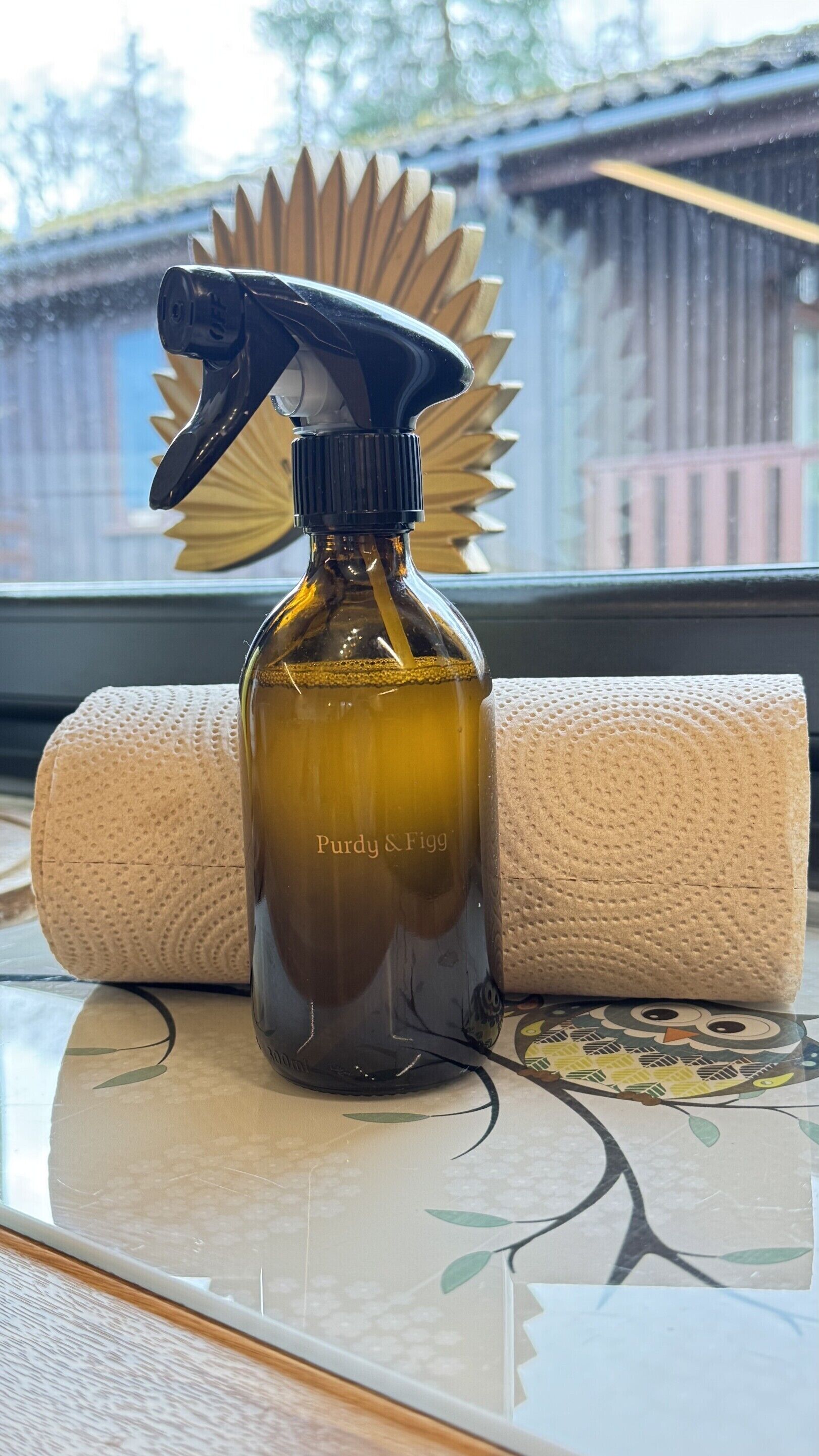 A spray bottle labeled "Purdy & Figg" on a table next to a rolled-up towel.
