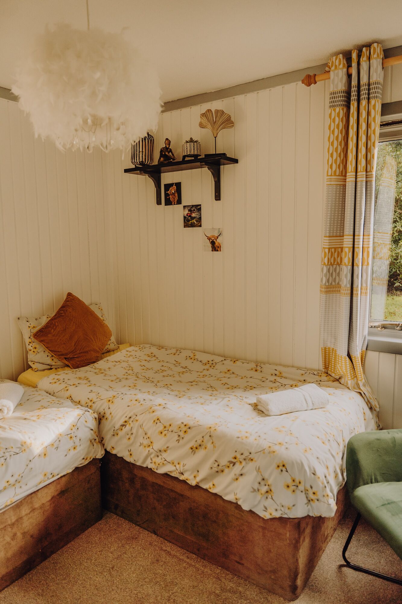 A bedroom with two beds, a shelf with decorative items, and a window with curtains.