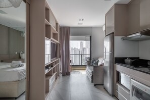 Quarto de hotel moderno com cama, sofá, cozinha e vista para a cidade.