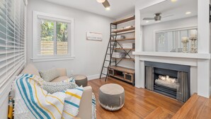 Un salon moderne doté d’une cheminée, de parquet, d’un canapé avec des coussins, d’un pouf rond et d’étagères intégrées.