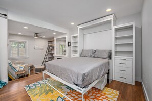 A bedroom with a bed, built-in storage, a ladder, a desk, and a window with blinds.