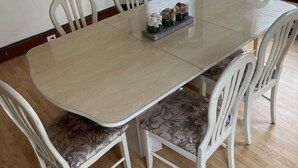 Una mesa de comedor con cuatro sillas, un banco estampado con motivos florales y una bandeja con objetos decorativos.