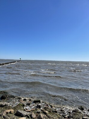 A rocky shoreline with waves crashing onto the beach and a pier extending into the water.