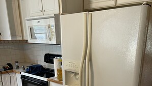 Una cocina con armarios blancos, un refrigerador blanco, un microondas y un horno.