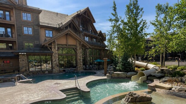 A hotel with a pool area featuring a hot tub, a slide, and a stone-tiled deck. - Ski-in/out Grand Lodge Peak 7 Suite. (Breckenridge)