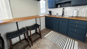 A kitchen with dark blue cabinets, a wooden countertop, a sink, and two stools.