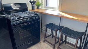 A kitchen with a black stove, two wooden stools, and a window with a plant on the windowsill.