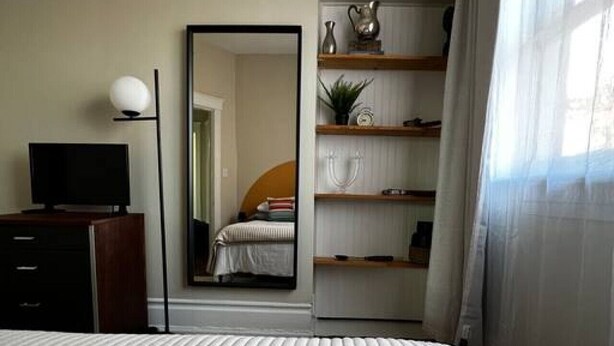 A neatly arranged bedroom with a bed, a TV, a mirror, and shelves with various items.