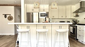 Una cocina moderna con taburetes blancos, una isla central, electrodomésticos de acero inoxidable y techo de madera.
