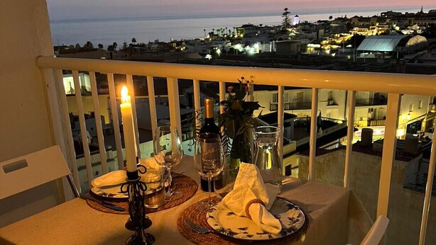 A balcony table set with dinnerware, a bottle, and glasses, overlooking a cityscape at dusk. - AP379 - Casa Seger - Parador (Nerja)
