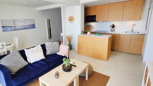 A modern living room with a blue sofa, a dining table with chairs, and a kitchen area with wooden cabinets and a microwave. - AP379 - Casa Seger - Parador (Nerja)