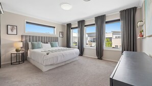 A modern bedroom with a large bed, a bedside table, a lamp, and a view of the outside through large windows. - Putt Putt - Pool Slide - 100m to Beach - Ultimate Family Entertainer (Kingscliff)