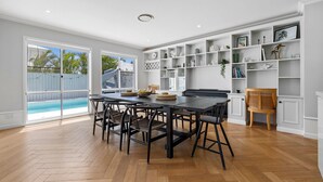 A spacious kitchen with a large dining table, white cabinetry, and a view of a swimming pool. - Putt Putt - Pool Slide - 100m to Beach - Ultimate Family Entertainer (Kingscliff)
