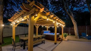 A covered outdoor patio with wooden beams, string lights, a hot tub, and a dining area.