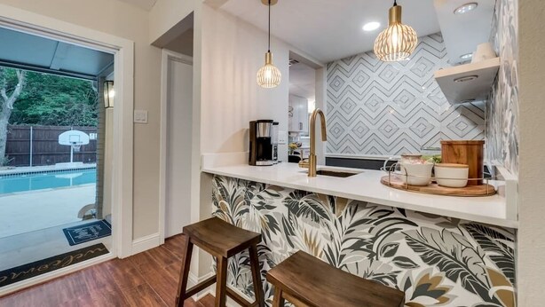 A modern kitchen with a white countertop, two hanging pendant lights, and a patterned backsplash.