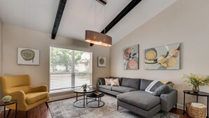 A modern living room with a sofa, armchair, coffee table, and artwork on the walls.