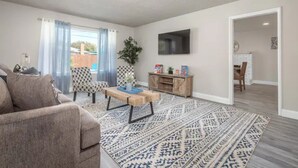 Ein modernes Wohnzimmer mit einer Couch, einem gemusterten Teppich und einem flachbildfernseher an der Wand.