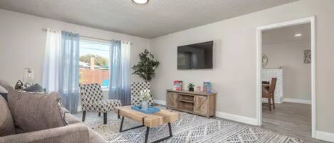 A modern living room with a sofa, patterned rug, and a flat-screen TV mounted on the wall.
