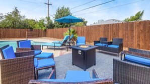 Eine Terrassengartenanlage mit Korbmöbeln, einem Feuerkorb und einem Pool.