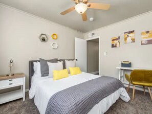 Un dormitorio con cama, mesita de noche, silla y una obra de arte en la pared.