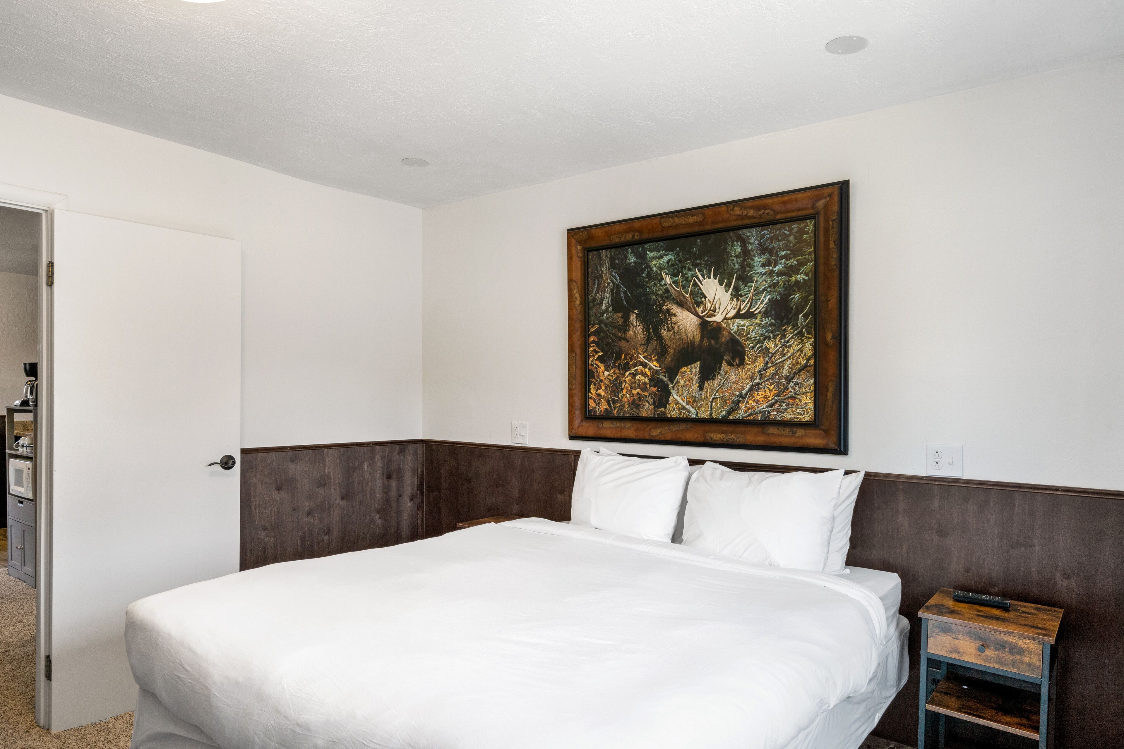 Ein Hotelzimmer mit einem großen Bett, einem hölzernen Kopfteil, einem Nachttisch und einem Bild eines Elchs an der Wand.