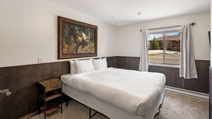 Habitación de hotel con una cama grande, un cuadro de un alce, una ventana con cortinas y vistas a un edificio.