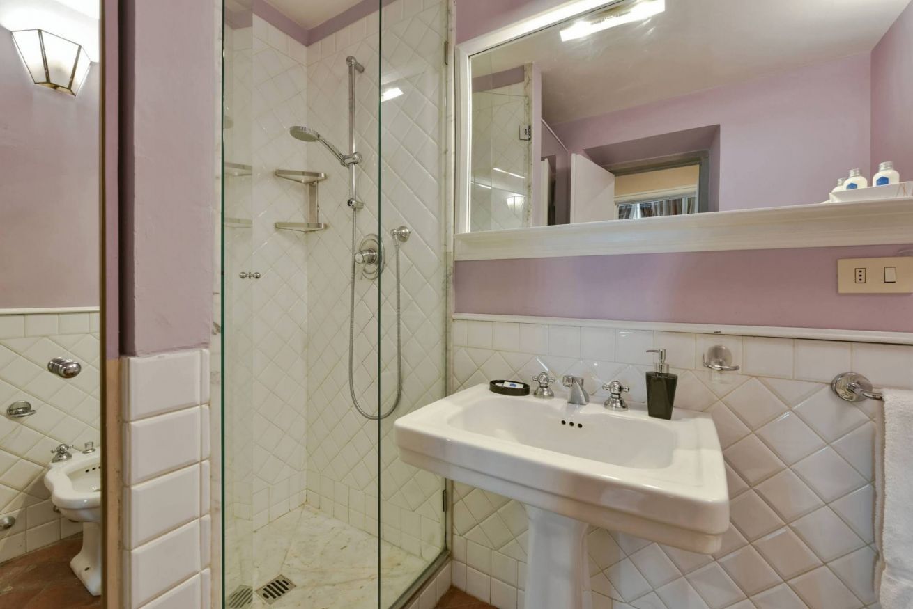 A bathroom with a glass-enclosed shower, a pedestal sink, and a mirror above the sink.
