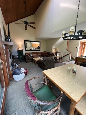 Un vaste salon doté d’un haut plafond, d’un ventilateur de plafond, d’une grande fenêtre et d’un coin repas avec une table et des chaises.